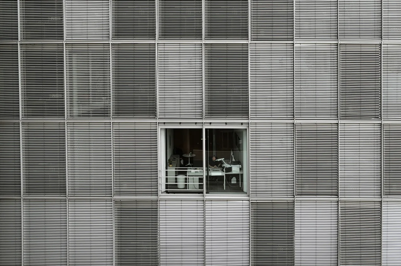 Façade d'un immeuble de bureaux aux stores baissés, une seule fenêtre ouverte